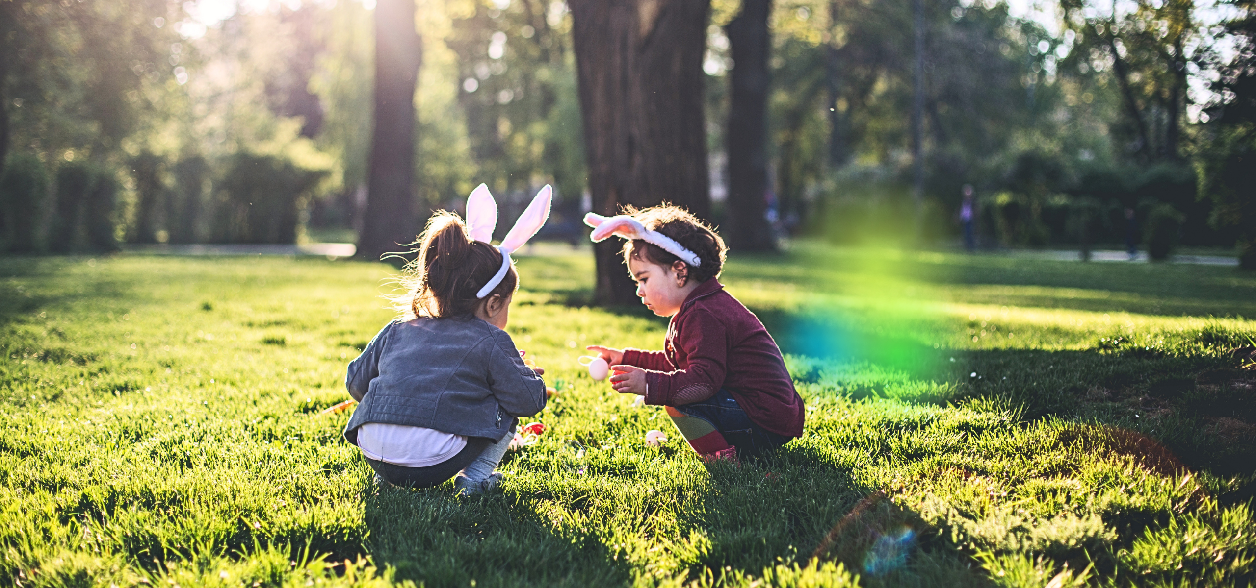 Kinder die auf einer Wiese zu Ostern Eier suchen.