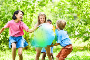 Glückliche Kinder draußen beim Spielen mit einem großen, aufblasbarem Globus. Sie entdecken die Welt und Energiegemeinschaften.